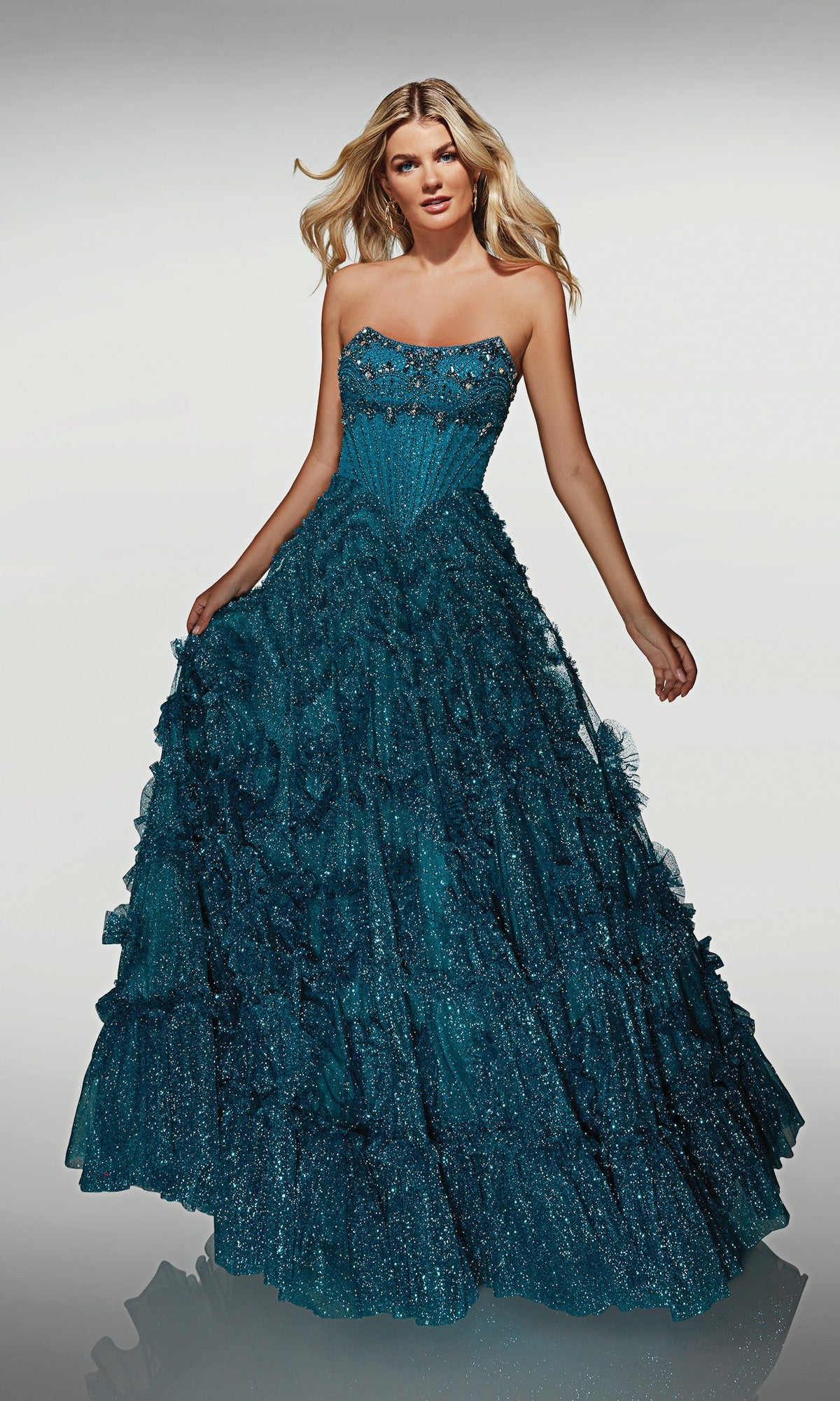 A woman wearing the Alyce 62132 long formal dress—a strapless teal gown with a ruffled, glitter tulle skirt—stands against a plain light background.